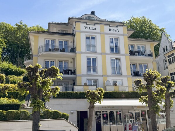 A multi-story building named "Villa Rosa" with balconies, a storefront, and well-maintained greenery.