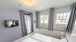 A hotel room with a bed, a television mounted on the wall, and windows with curtains. - MR: Villa Rosa Whg. 16 Sea magic with 2 roof terraces - Villa Rosa Whg. 16 (Sellin)