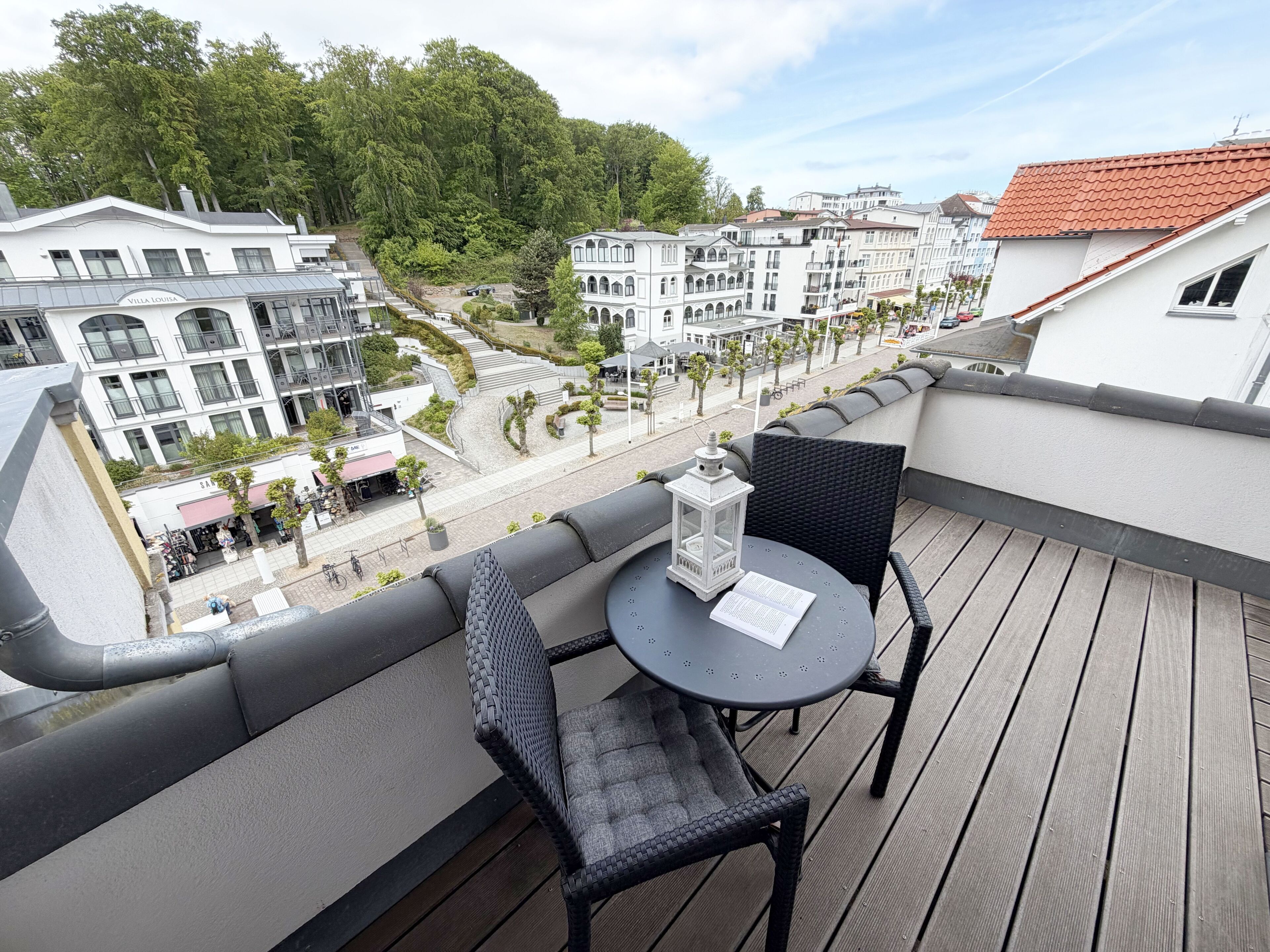 Een balkon met een tafel en stoelen, met uitzicht op een straat met gebouwen en bomen.