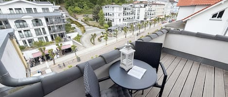 Un balcon avec une table et des chaises, donnant sur une rue bordée d’immeubles et d’arbres.