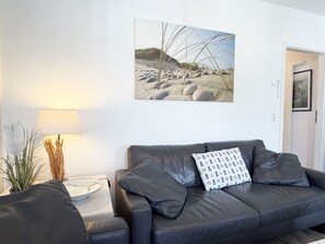Uma sala de estar moderna com um sofá de couro, uma mesinha redonda, uma luminária e um quadro pendurado na parede.