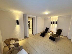 Um quarto espaçoso com uma janela grande, um espaço de estar com duas cadeiras e uma mesa, e uma área de relaxamento separada com uma poltrona e uma mesa pequena.