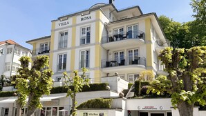 A multi-story hotel named Villa Rosa with balconies and a sign indicating a 2-minute walk to a bus stop. - MR: Villa Rosa Whg. 16 Sea magic with 2 roof terraces - Villa Rosa Whg. 16 (Sellin)
