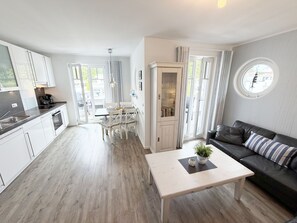 A modern kitchen with white cabinets, a dining area with a table and chairs, and a living room with a sofa and a coffee table. - MR: Villa Rosa Whg. 16 Sea magic with 2 roof terraces - Villa Rosa Whg. 16 (Sellin)