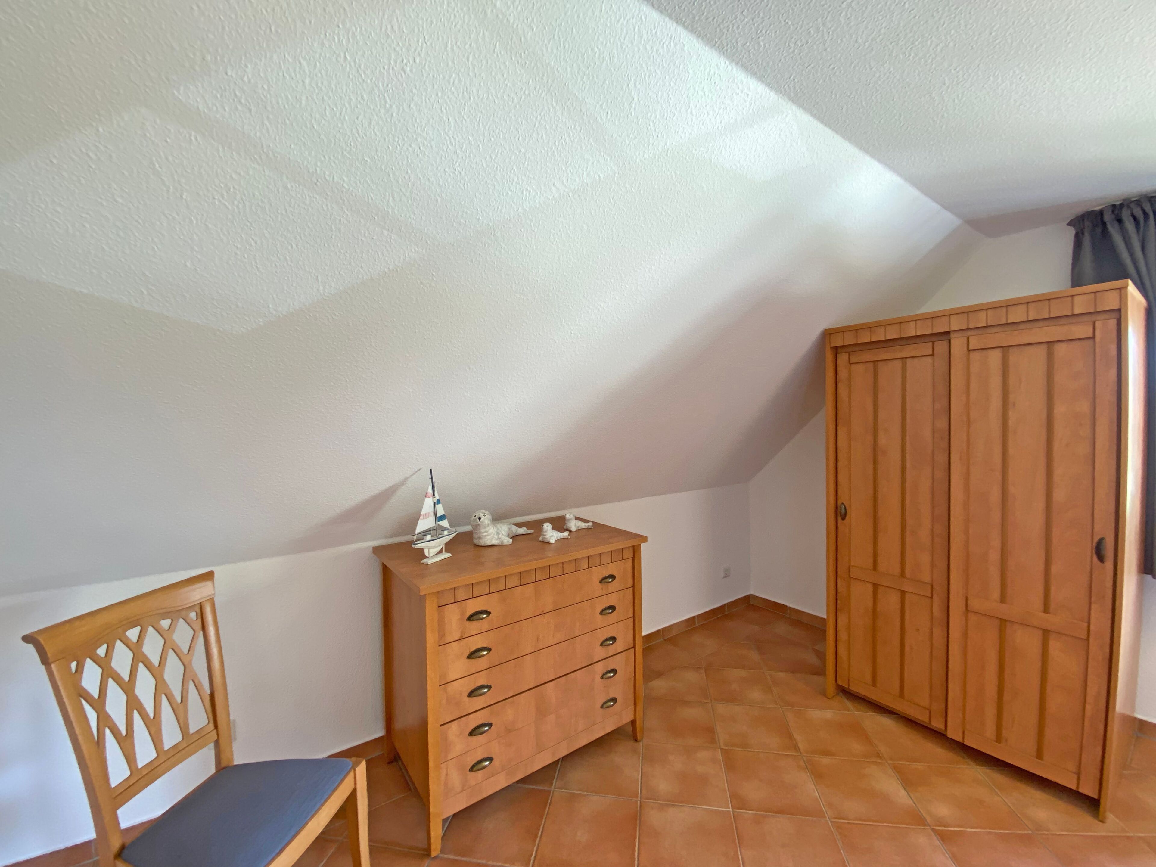 A room with a wooden dresser, a chair, and a wardrobe.