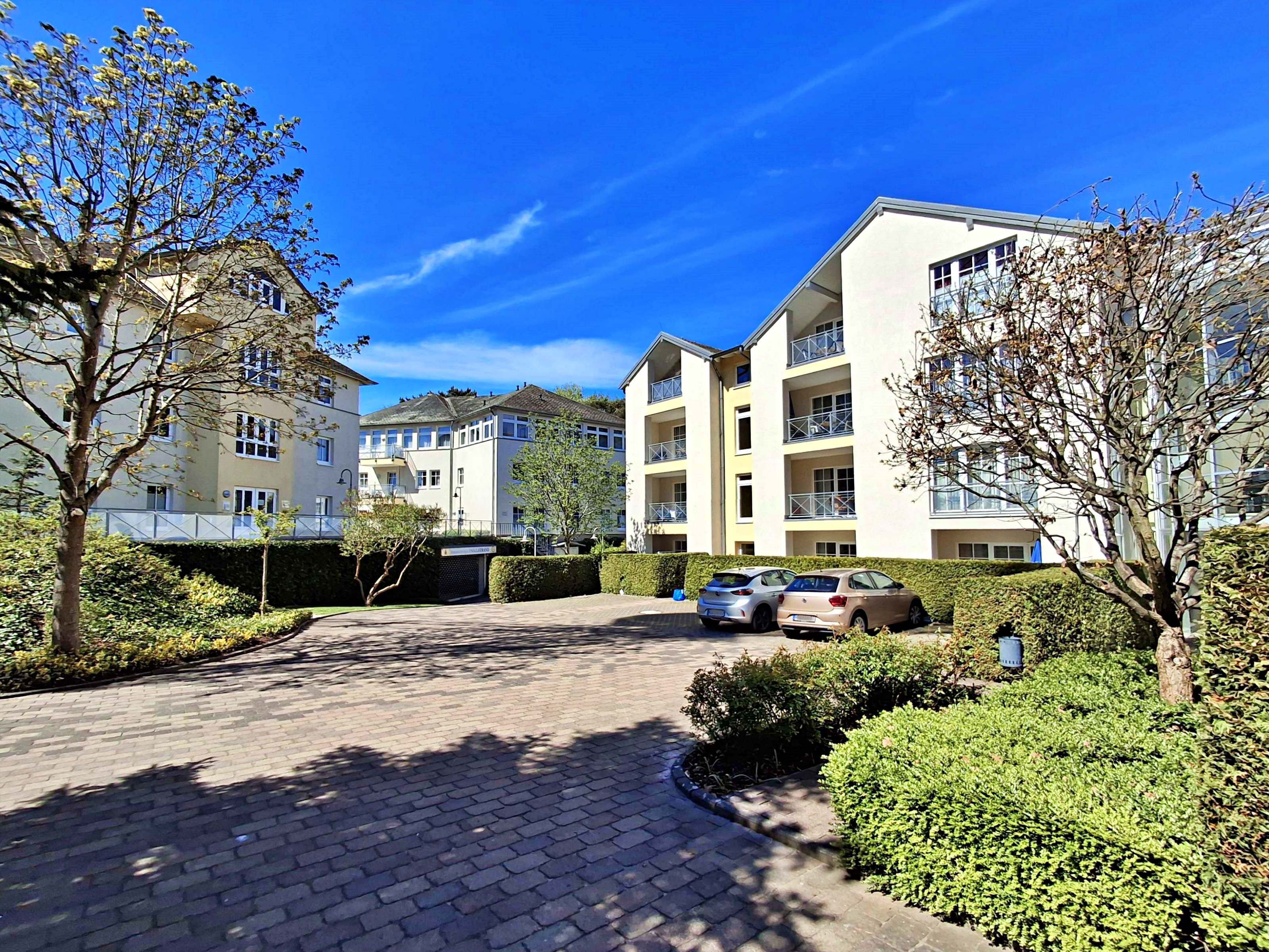 A residential building with multiple balconies, a paved driveway, and surrounding greenery.