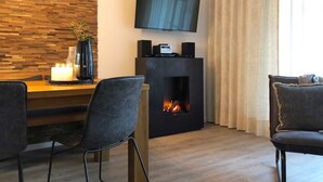 Een moderne woonkamer met een open haard, een flatscreen televisie aan de muur en een eethoek met twee stoelen en een tafel.