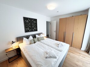 A bedroom with a large bed, a wooden wardrobe, and a wall-mounted decorative panel. - Apartment 1. 18 island beach - Apartment 1. 18 (Heringsdorf)