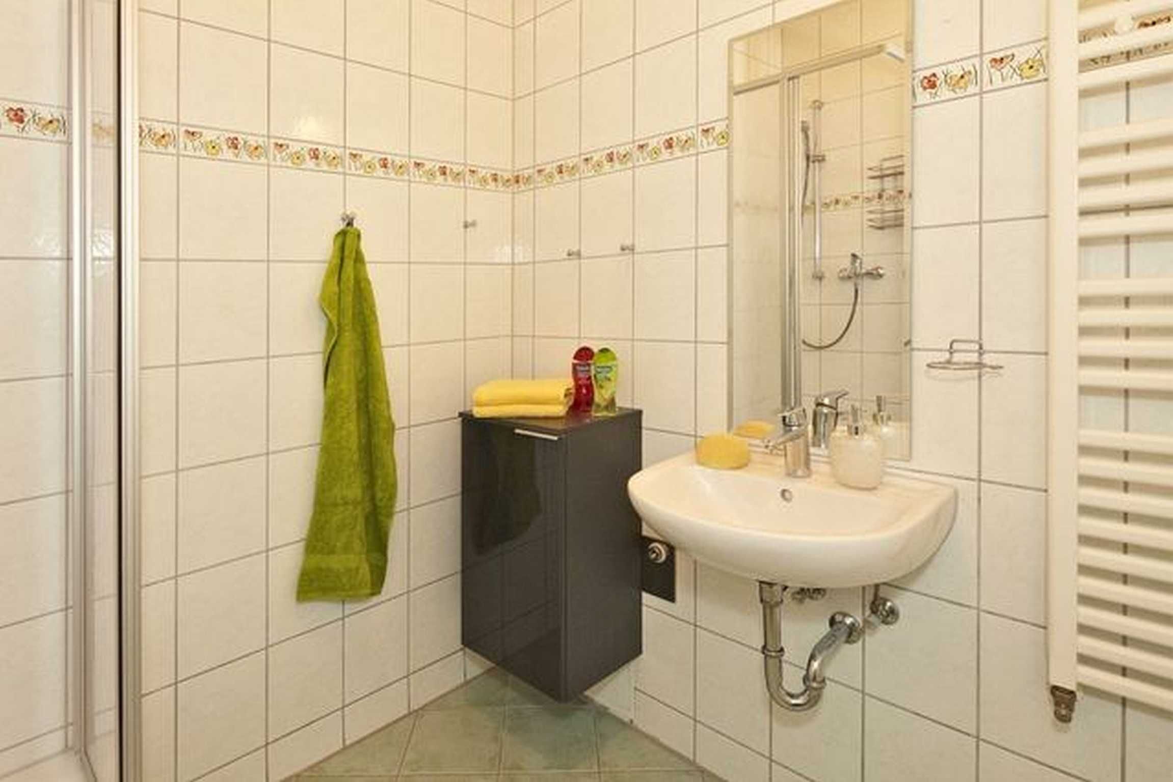 A bathroom with white tiled walls, a sink with toiletries, a shower, and a towel rack.