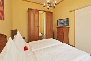 A hotel room with a bed, wooden wardrobe, a television on a wooden stand, and a chandelier. - Apartment Silvia - House Prussia (Heringsdorf)