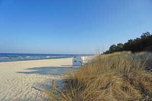 Une plage avec une structure blanche portant l’inscription « M3 » au premier plan, une plage de sable et l’océan en arrière-plan.