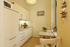 A compact kitchen with white cabinets, a wooden table, and a small dining area. - Apartment Silvia - House Prussia (Heringsdorf)