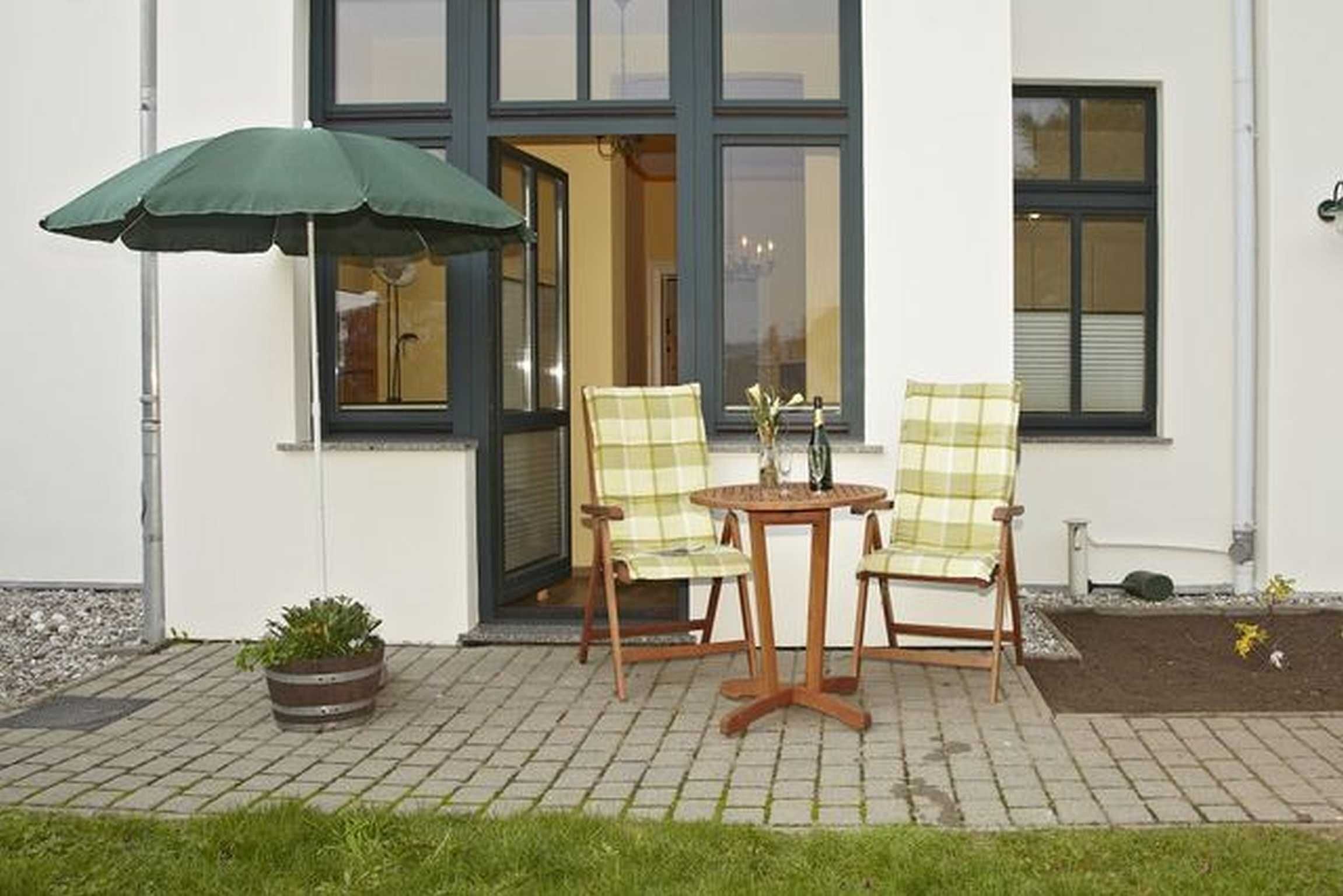 A patio with two chairs and a table, a green umbrella, and a potted plant.