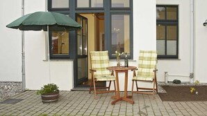 A patio with two chairs and a table, a green umbrella, and a potted plant.