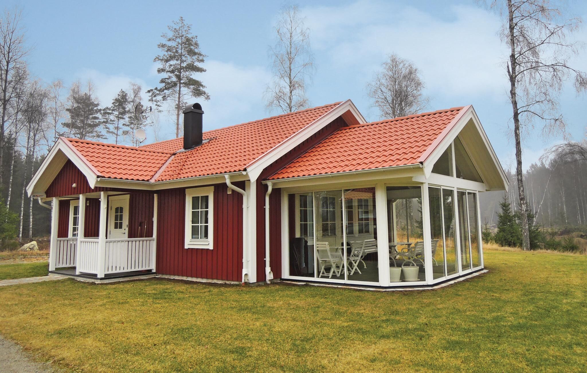 A red and white wooden house with a glass conservatory, surrounded by a grassy yard and trees.