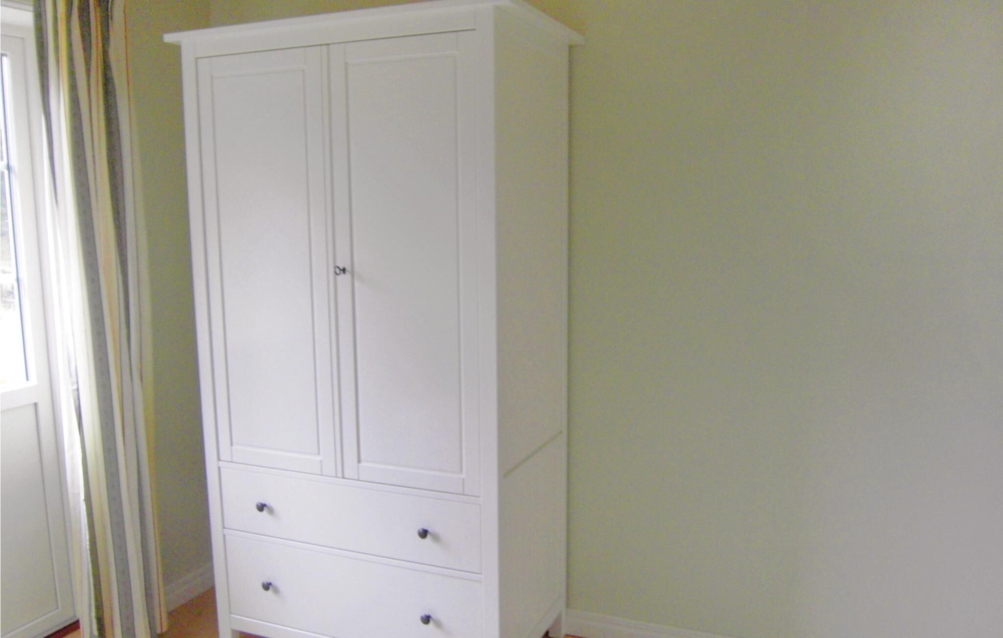 Ein weißer Kleiderschrank mit zwei Türen und drei Schubladen.