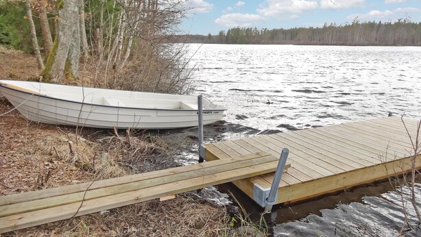A wooden dock extending into a lake with a small boat docked at the end. - Lovely home in Ryd with sauna (Ryd)
