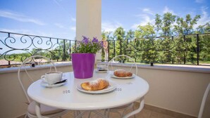 A balcony with a white table, two chairs, a purple flower pot, a cup of coffee, and two pastries. - Holiday apartment with pool (Nova Vas/Poreč)