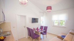 A dining area with a table set for four, purple chairs, a TV mounted on the wall, and a window with blinds. - Holiday apartment with pool (Nova Vas/Poreč)