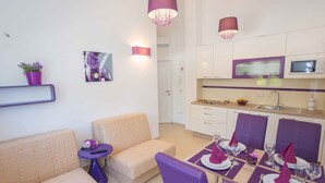 A modern living room with a sofa, a small table with a remote control, and a dining area with purple chairs and a table set for two. - Holiday apartment with pool (Nova Vas/Poreč)