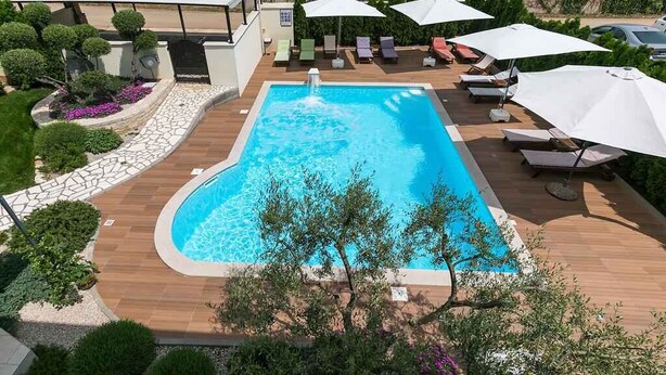 A rectangular swimming pool with a built-in hot tub, surrounded by wooden decking and white umbrellas. - Holiday apartment with pool (Nova Vas/Poreč)