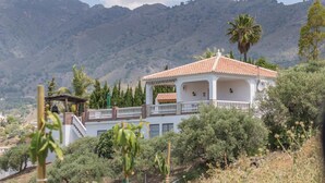 A white villa with a red-tiled roof, a balcony, and a view of mountains.