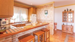 A kitchen with wooden cabinets, a central island with stools, a refrigerator, and a microwave.