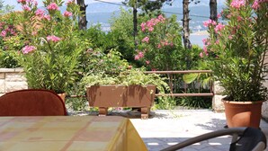 Un patio con mesa y sillas, rodeado de plantas y flores en macetas, con vistas a un paisaje pintoresco.
