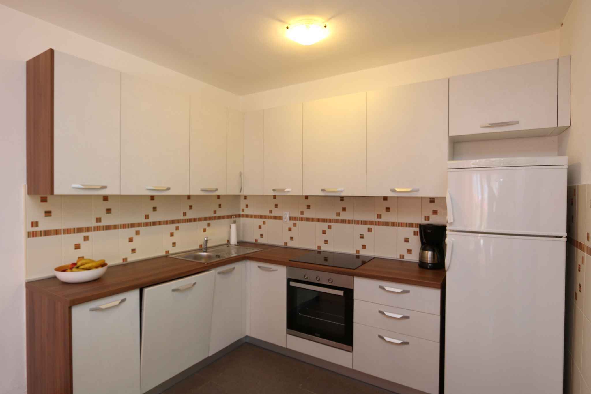 A compact kitchen with white cabinets, a wooden countertop, a built-in oven, and a refrigerator.