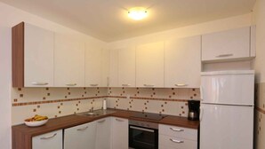 Una cocina compacta con armarios blancos, una encimera de madera, horno integrado y refrigerador.