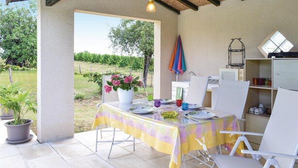 Een overdekt terras met een eettafel, plantenpotten en uitzicht op een wijngaard.