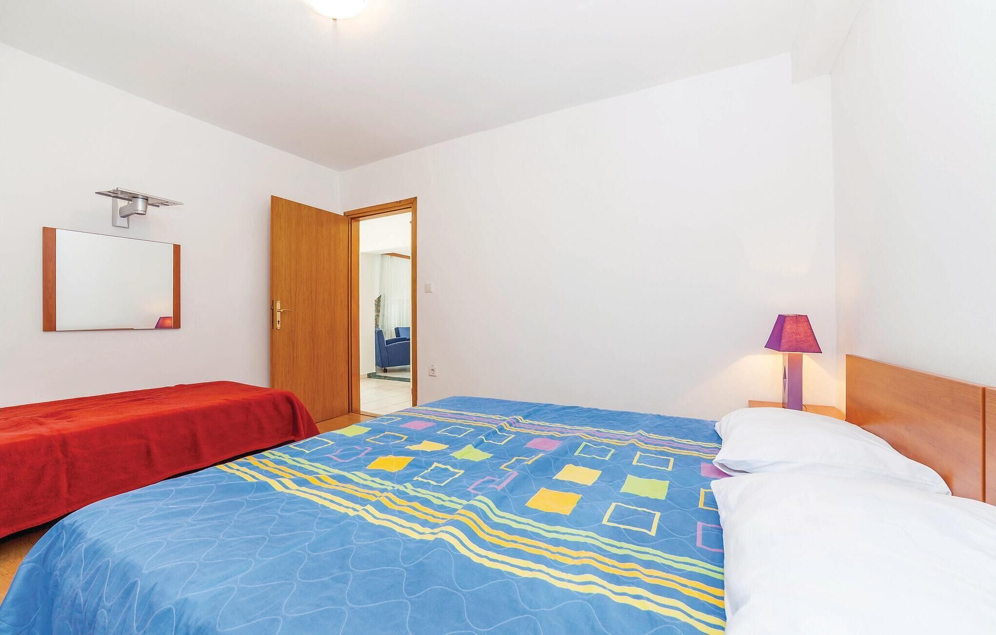 A hotel room with a bed, a red chair, a wooden door, a mirror, and a lamp.