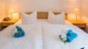 A hotel room with two beds, white linens, and decorative towels with flowers.