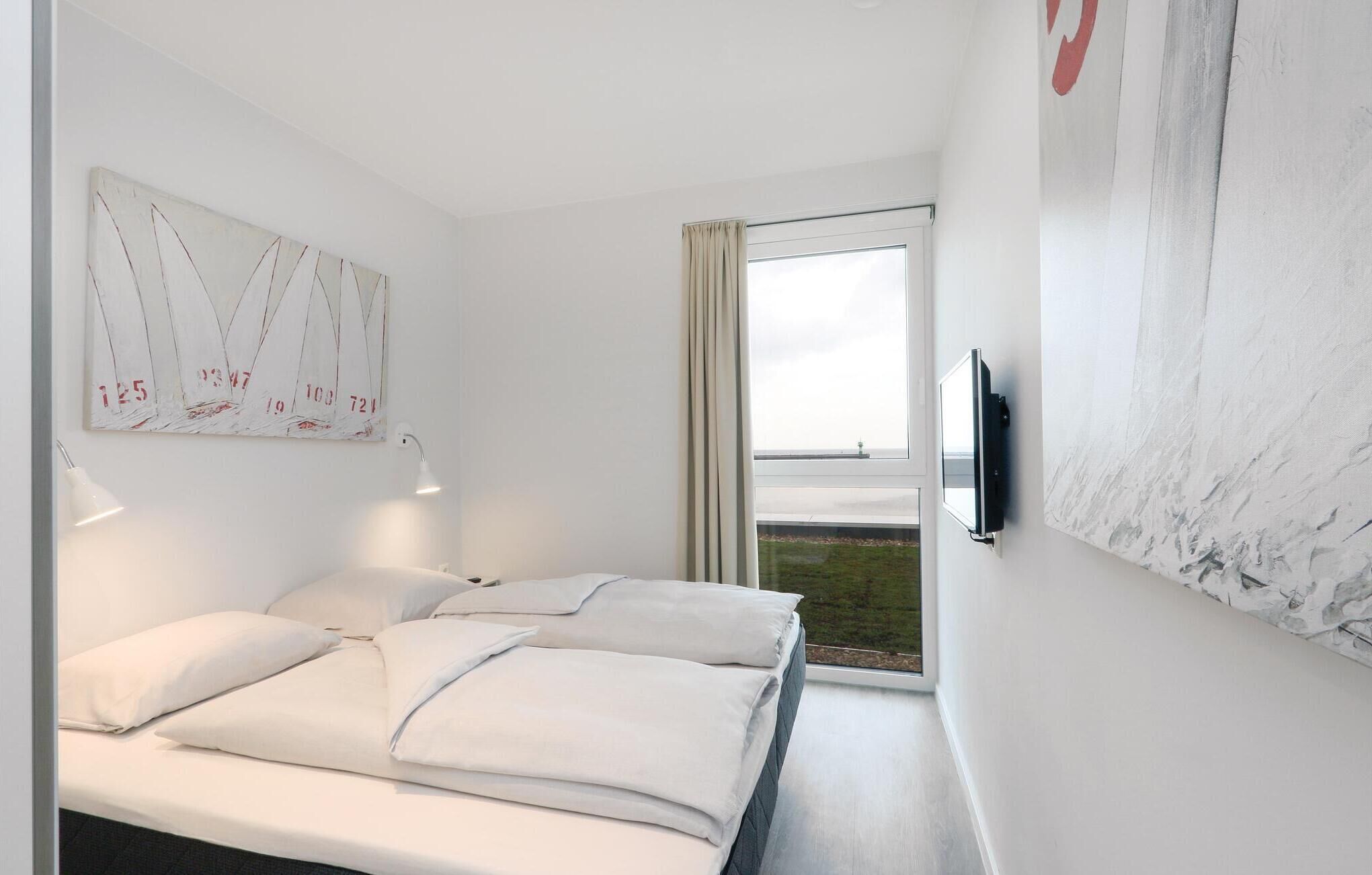 Una habitación de hotel moderna con una cama, un televisor montado en la pared y un amplio ventanal con vistas al exterior.