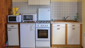 A compact kitchen with a microwave, toaster, coffee maker, stove, oven, and a sink with wooden countertop.