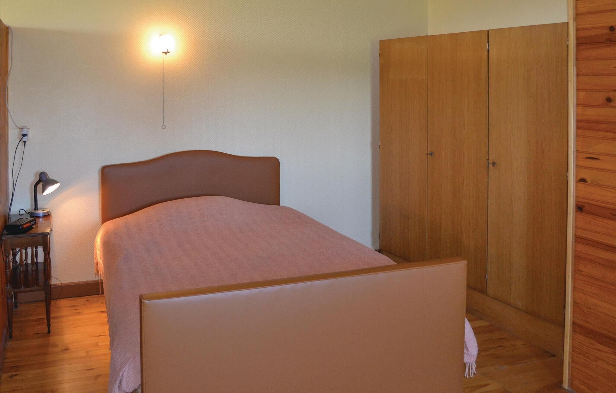 Een slaapkamer met een bed, nachtkastje met lamp, een houten garderobe en een wandlamp.
