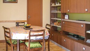 A dining area with a round table, four wooden chairs, a floral tablecloth, and a bowl of fruit.