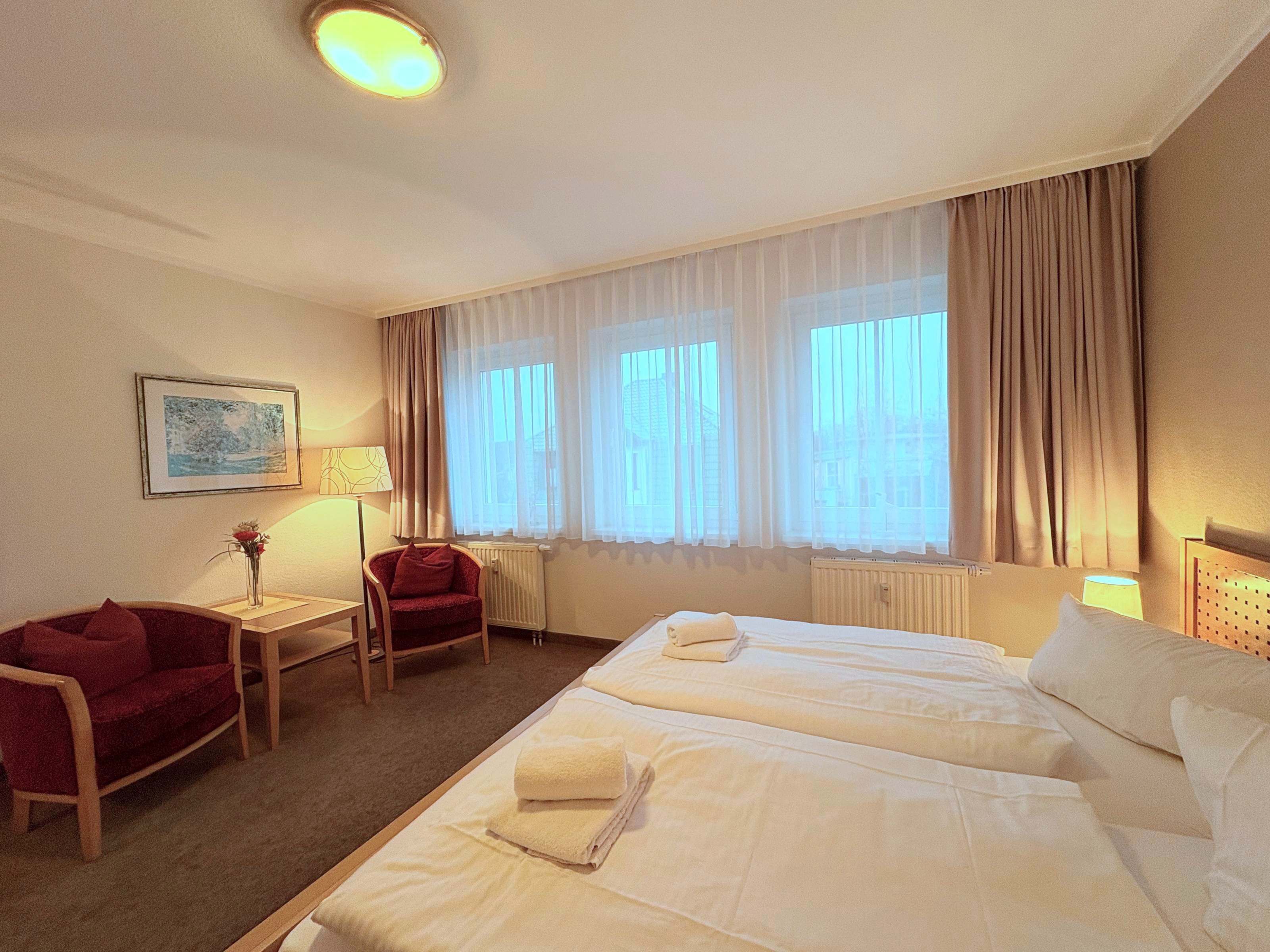 A hotel room with two beds, a chair, a table, and a window with curtains.