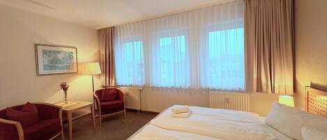 A hotel room with two beds, a chair, a table, and a window with curtains.