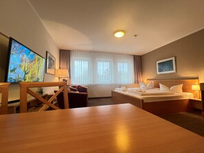 Une chambre d’hôtel avec un lit, un bureau, une chaise, une télévision et une fenêtre avec des rideaux.