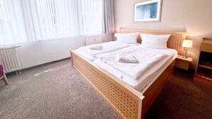 Una camera d'albergo con un letto grande, un termosifone, una finestra con tende leggere, un quadro appeso al muro e un comodino con una lampada.