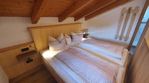 Une chambre avec un plafond en bois, un lit avec une literie à rayures, une table de chevet et un luminaire fixé au mur.