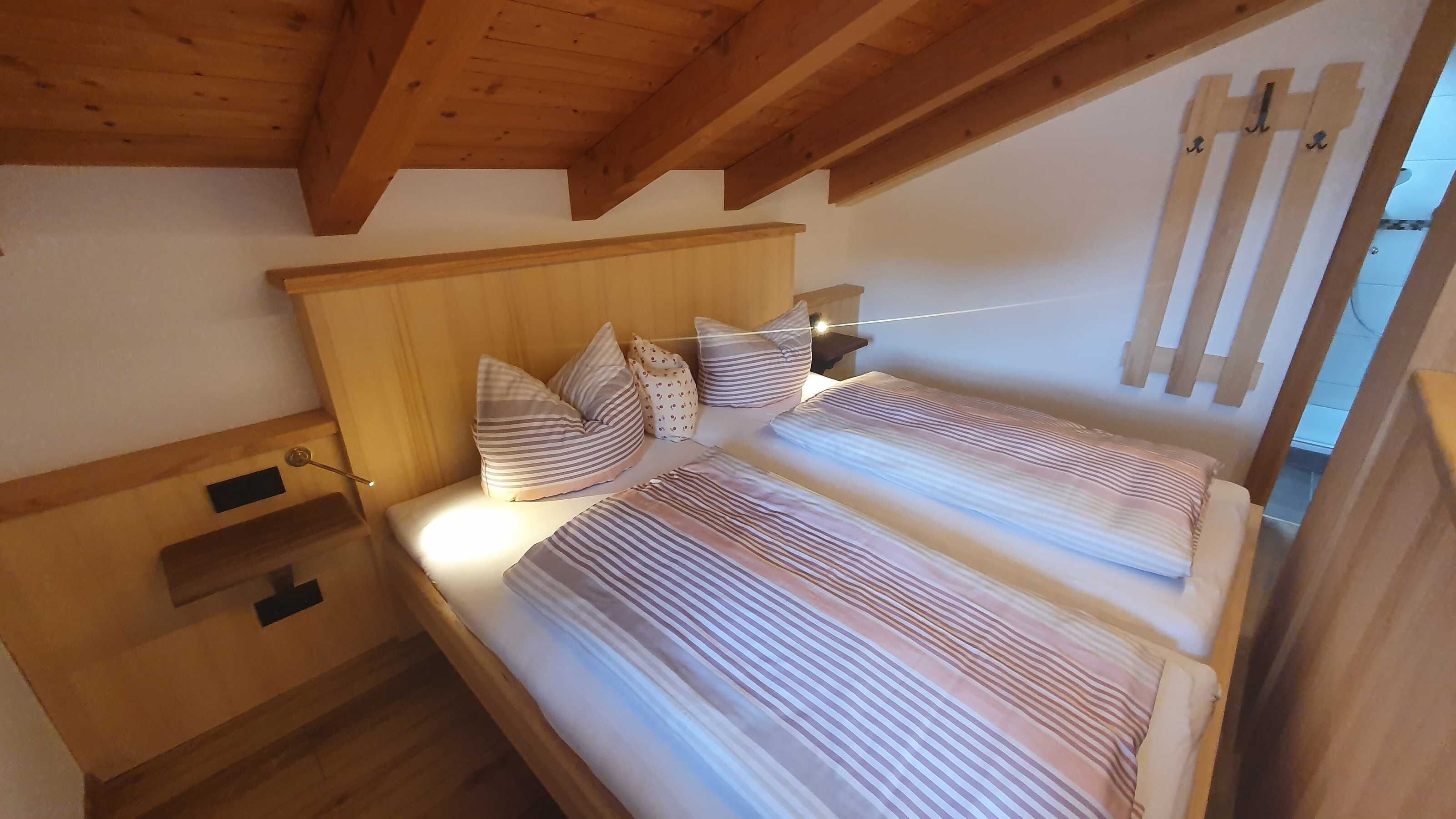 Een slaapkamer met een houten plafond, een bed met gestreept beddengoed, een nachtkastje en een wandlamp.