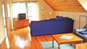 A cozy living room with a wooden ceiling, a blue sofa, a wooden coffee table, and a television on a wooden cabinet. - Cozy home in Strängnäs with sauna (Strängnäs)