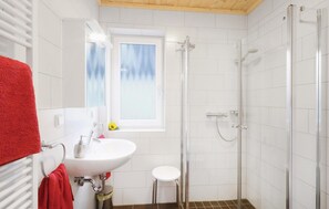 A bathroom with a white sink, a mirror, a red towel, a small stool, and a glass-enclosed shower.
