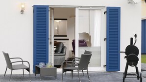 An outdoor seating area with two chairs and a table, a sliding glass door, and a barbecue grill.