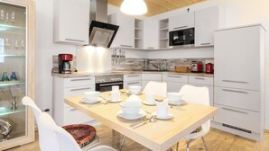 A modern kitchen with white cabinetry, a wooden dining table set for four, and a hanging light fixture.