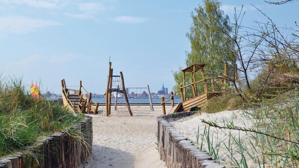 A sandy beach path leading to a wooden structure with a netted swing set.