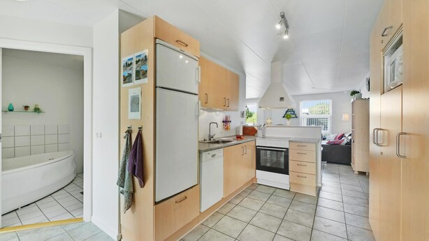 A compact kitchen with a refrigerator, oven, and sink. There is a window providing natural light and a view of the outdoors.
