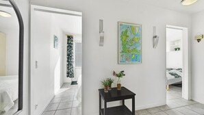 A hallway with a map, a small table with plants, and a bed in the background.
